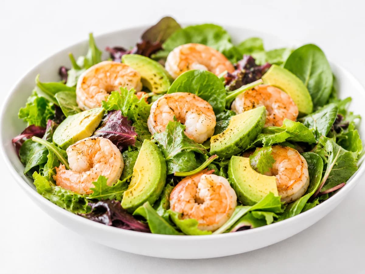 Plate of mixed greens with shrimp, avocado, and corn in a light lime dressing; top-down.
